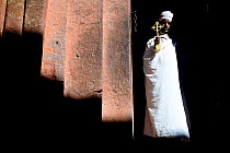 Priest in traditional white robes and turban, holding a gold cross. Bet Giyorgis Church, Lalibela. UNESCO World Heritage Site. Ethiopia, December 2014.