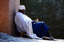 Christian worshiper in traditional white robes, resting against wall, Bet Medhane Alem (part of the northwestern group of churches in Lalibela). UNESCO World Heritage Site. Lalibela. Ethiopia, Decembe...