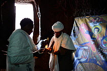 Devout Christian in traditional robess lighting candle in front of Bet Danaghel (part of the northwestern group of churches in Lalibela). UNESCO World Heritage Site. Lalibela. Ethiopia, December 2014.