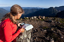 Woman navigating with the aid of GPS on a mobile phone, Boulder River Wilderness, Mount Baker-Snoqualime National Forest, Washington, USA. August 2014. Model released.