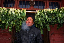 Man smoking cigarette, with hanging vegetable behind, Poyang Ho Lake, Jiangxi province, China