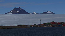 Wide angle shot of a wind turbine turning at Mawson Station, with mountains of the David Range in the background, Antarctica.