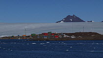 Mawson Station seen from a boat, with two wind turbines turning and mountains of the David Range in the background, Antarctica.