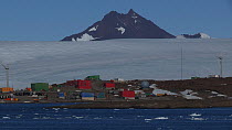 Mawson Station seen from a boat, with two wind turbines turning and mountains of the David Range in the background, Antarctica.