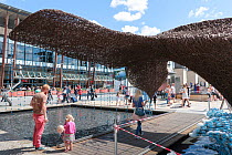 People in front of the The Bristol Whales - wicker sculpture of two Blue whales surfacing surrounded by plastic bottles. Art installation by Cod Steaks to mark the Bristol Green Capital 2015. Millenni...