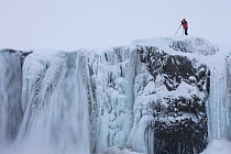 Photographer with tripod on edge of Godafoss warterfall, frozen in winter, Iceland, February 2014.