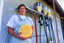 Cheesemaker holding a hard cheese, with equipment in the background. Triglav National Park, Slovenia, October 2014.