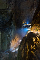 Tourist walking along illuminated footpath in Skocjan Caves, looking down into underground stream, Green Karst, Slovenia, Europe