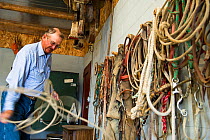 Bob Price tidying up the ropes in tack room where horse saddles and bridles are stored. Gracie Creek Ranch, Garfield County, Nebraska, Mid-West United States of America.