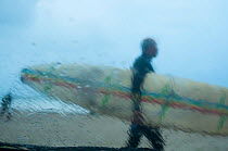 Surfers walking to sea with board on beach, viewed through rain covered window, Surfers Corner, Muizenberg Beach, False Bay, near Cape Town, Western Cape, South Africa. June 2011.