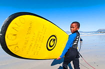 Young boy surfer with board, Surfers Corner, Muizenberg Beach, False Bay, near Cape Town, Western Cape, South Africa. June 2011.