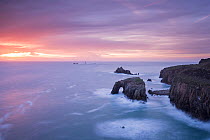 View towards Enys Dodnan Arch and the Armed Knight rock at sunset,  with Longships lighthouse in the distance, Land's End, Cornwall, UK. March 2015.