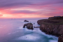 View towards Enys Dodnan Arch and the Armed Knight rock at sunset, with Longships lighthouse in the distance, Land's End, Cornwall, UK. March 2015.