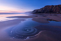 Long exposure of Sandymouth Bay, at dusk showing eddies in the water, Bude, Cornwall, UK. April 2015.