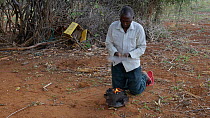 Man wafting a small charcoal fire to increase airflow, Kenya, 2014.