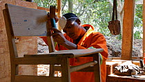 Man building a chair in a workshop in a sustainable timber yard, Mezimbite Sustainable Forest Camp, Mozambique, 2014.