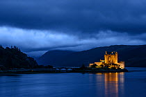 Eilean Donan Castle lit up at twilight with dark clouds. Scotland, UK, September 2013.