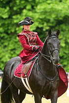 Lady dressed in period costume rides side saddle a rare black Kladruber horse/stallion, at the Great Riding festival, in Slatinany national stud, Pardubice Region, Czech Republic. June 2015.
