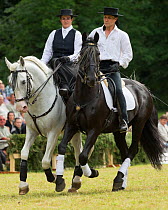 Two riders, dressed in Spanish period costume, ride two rare Kladruber horses/stallions (one black, one white), at the Great Riding festival, in Slatinany national stud, Pardubice Region, Czech Republ...
