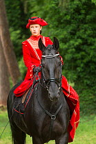 Lady dressed in period costume, riding rare black Kladruber stallion side saddle, at the Great Riding festival, in Slatinany national stud, Pardubice Region, Czech Republic. June 2015.