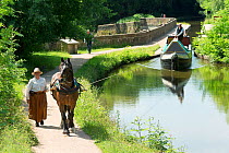 Sue Day, in a Victorian dress, tows with her draft horse, Maria, a 1814 wooden narrowboat, on the canals, near Marple, Metropolitan Borough of Stockport, Greater Manchester, England. July 2015.