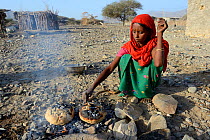 Afar tribe woman baking bread with hot stone on open fire, Malab-Dei village, Danakil depression, Afar region, Ethiopia, March 2015.
