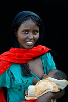 Afar woman with tattoos / skin scarification on her face breastfeeding her baby, Danakil depression, Afar region, Ethiopia, March 2015.