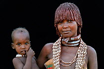 Young Hamer tribe woman with baby, wearing traditional necklaces and hair covered with a mixture of ochre and animal fat, Omo valley,  Ethiopia, March 2015.