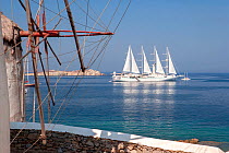 Traditional windmill, and luxury ship Wind Star, which is a sleek, 4-masted sailing yacht. Mykonos Island, Cyclades, Aegean Sea, Mediterranean, Greece, August 2007