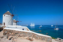 Traditional windmills, and luxury yachts, including the luxury ship Wind Star, which is a sleek, 4-masted sailing yacht. Mykonos Island, Cyclades, Aegean Sea, Mediterranean, Greece, August 2007
