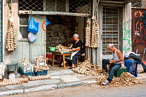 Husband and wife string garlic (Allium sativum) in warehouse to sell at markets. Attica region, Athens, Greece, Mediterranean, October 2013
