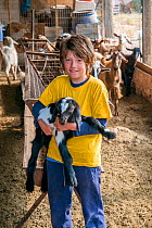 Young boy holding a small baby Domestic goat (Capra aegagrus hircus) Spetses Island. Spetses Island, Aegean Sea, Greece, Mediterranean, August.