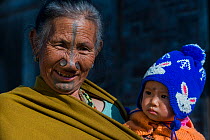 Apatani woman with facial tattoos and traditional nose plugs / Yapin Hulo holding baby. These plugs are made of a cane slice. This practice was to make them look unattractive to males from other tribe...