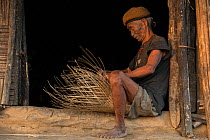Konyak Naga tattooed head hunter making a basket. Only someone who has killed and taken a human head can be tattooed in this manner. Mon district. Nagaland,  North East India, October 2014.