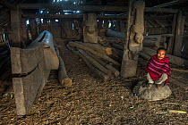 Konyak Naga man crouching by Hongphoi Village Log drum. Mon district. Nagaland,  North East India, October 2014.