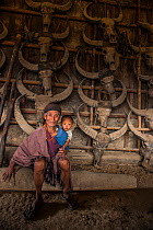 Konyak Naga man with grandson, in house decorated with buffalo skulls, Mon district, Nagaland, North East India, October 2014.