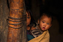 Konyak Naga children peering round doorway, Mon district, Nagaland, North East India, October 2014.
