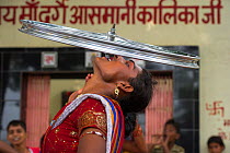 Hijra performer, balancing bicycle wheel on teeth. Hijra are transgender people, legally recognized as a third gender in India.  Uttar Pradesh, India, October 2014.