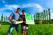 Man and woman holding a small crate of produces and a sign at an organic farm, Les Terres du Vancon, Les Demesses, Volonne, Val de Durance, Alpes Haute Provence, France, June.