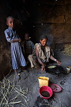 Woman preparing coffee in hut, with child,  Shesher lake, Fogera Plains, Lake Tana Biosphere Reserve, Ethiopia. December 2013.