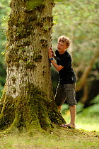 Boy standing next to Oak tree (Quercus) Bolderwood Arboretum Ornamental Drive in Lyndhurst, Hampshire, UK, July. Model released.