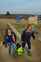 British Divers Marine Life Rescue animal medics Michelle Clement and Rachel Shorland carry a very weak, injured, grey seal pup (Halichoerus grypus) 'Jenga', in a bag after rescuing it from Black Rock...