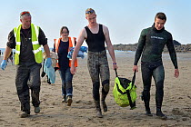 British Divers Marine Life Rescue animal medics Simon Dolphin and Michelle Clement accompanying people carrying an injured Grey seal pup (Halichoerus grypus) 'Boggle' in a ventilated rescue bag, Crack...