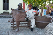 Cuban man reading a newspaper, sitting with statue of himself in the same pose. The government of Camaguey commissioned sculptures of normal citizens around the town.  Plaza del Carmen, Camaguey, Cuba...