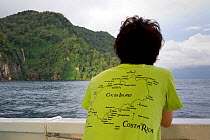 Tourist looking out towards waterfall on the coast, from the Wind Dancer, luxury liveaboard boat, Cocos Island National Park, Costa Rica, East Pacific Ocean. September 2012.