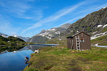 Ovre Pikhaugvatnet Lake with a small hut, Pikhaughytta, on the bank, and a man crouched by he water, Glomdalen Valley, Saltfjellet-Svartisen National Park, Norway, August 2015.