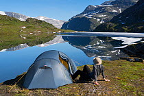 Woman sitting outside tent on the edge of the Ovre Pikhaugvatnet lake,  Saltfjellet-Svartisen National Park, Norway, August 2015.