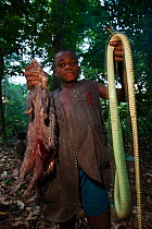 Baka boy holding up Mamba snake (Dendroaspis sp) and African brush tailed porcupine (Atherurus africanus) killed during hunt, South East Cameroon, July 2008.