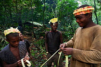 Baka man with three boys making plant fiber crowns for a night ceremony, South East Cameroon, July 2008.