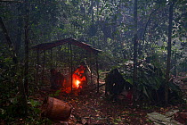 Two Baka people sitting by fire in hunting shelter, in rain, Cameroon, South East Cameroon, July 2008.